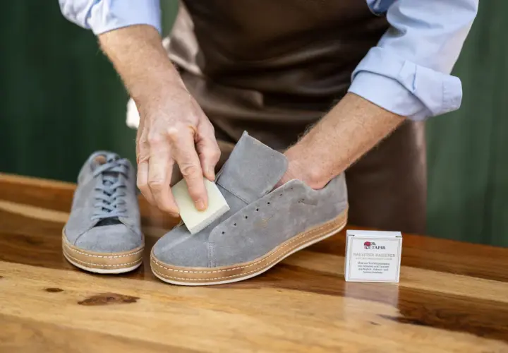 Mann reinigt graue Nubukleder-Sneaker mit einem speziellen Radierer. Die richtige nubukleder pflege erhält die Schuhe.