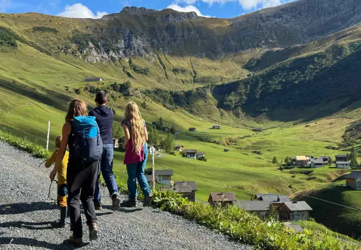 Familie genießt das Liechtenstein wandern in den Alpen. Grüne Hänge, kleine Häuser und ein Bergpanorama.