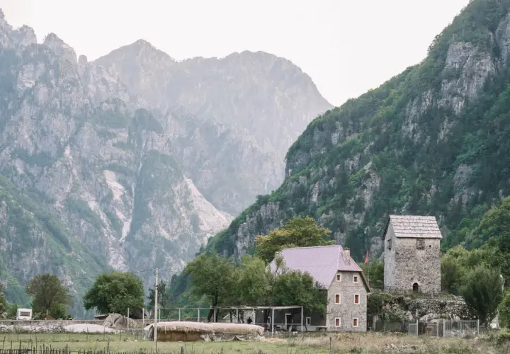 Steinerne Häuser und ein alter Turm in Albanien Theth, umgeben von majestätischen, nebelverhangenen Bergen.