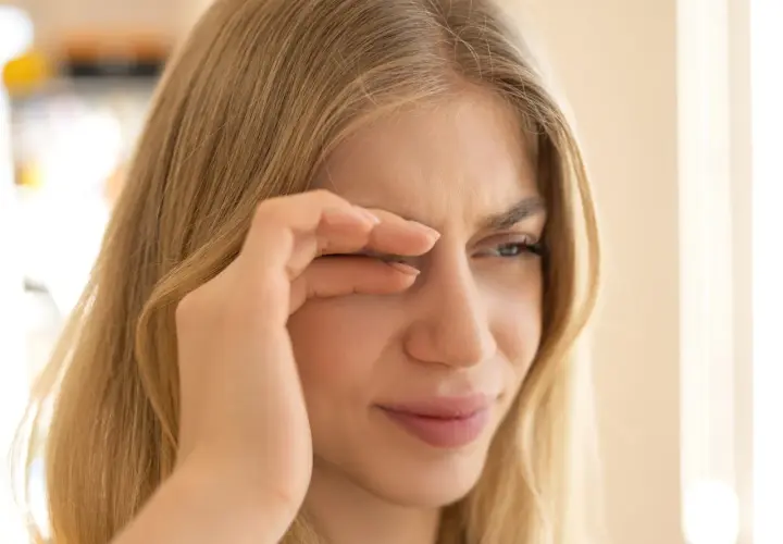Junge Frau reibt sich die Augen, weil sie flimmern vor den Augen hat. Wahrscheinlich hat sie zu wenig getrunken.