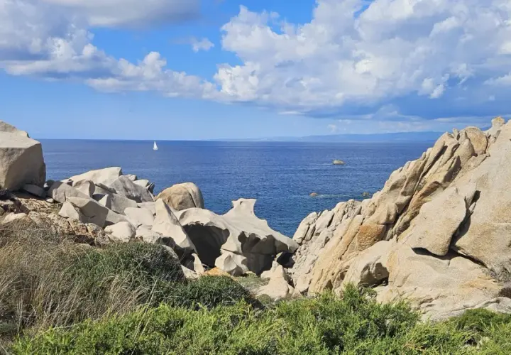 Felsformationen am Capo Testa, Sardinien, mit Blick auf das blaue Meer und eine einsame Segelyacht.