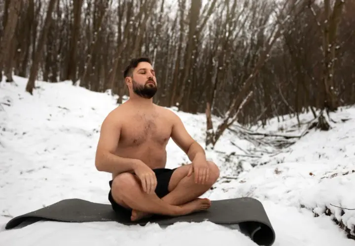 Mann in der Natur, barbusig im Schnee sitzend, praktiziert Wim Hof Atmung.
