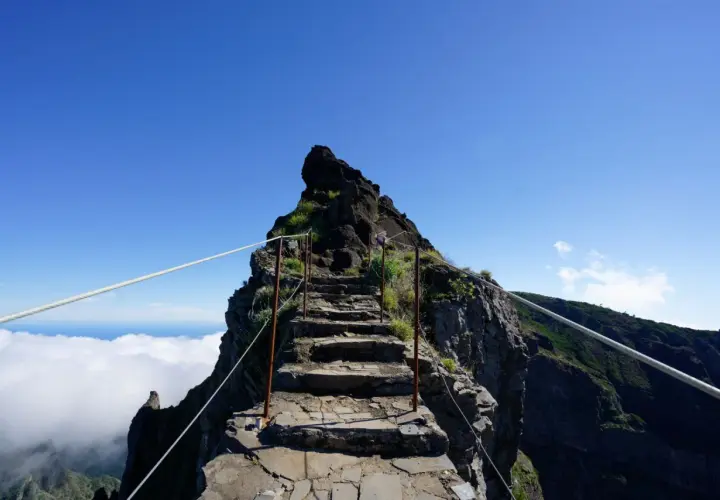 Steile Steintreppe, die sich den Berg hinaufwindet, mit Seilen gesichert. Eine Himmelsleiter auf Madeira, die über den Wolken in den blauen Himmel führt.