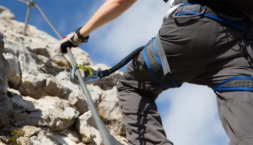 Person klettert gesichert an einem Stahlseil. Die Klettersteig Sicherung ist deutlich sichtbar.