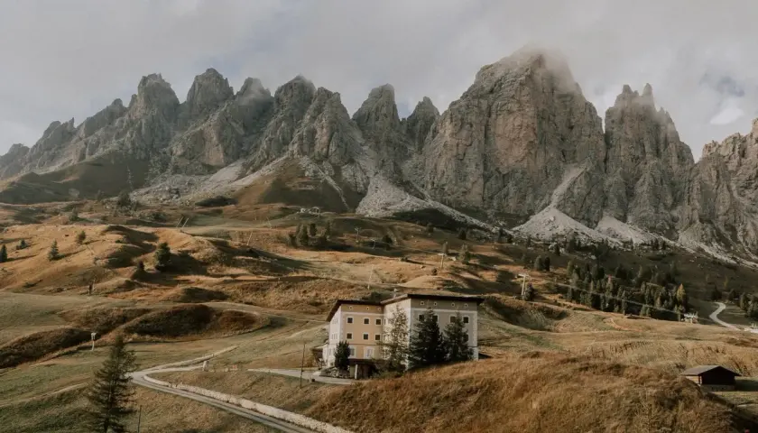 Majestätische Berge im Val di Funes, ein Hotel auf einem Hügel, umgeben von herbstlichem Gras und einer Straße.