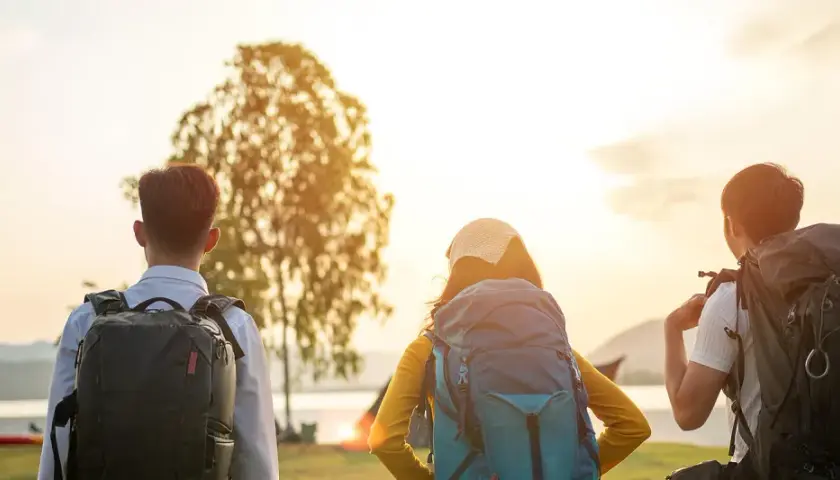 Drei Rucksackträger blicken auf den Bodensee. Die Sonne geht unter und taucht die Landschaft in warmes Licht. Eine perfekte Wanderung am Bodensee.