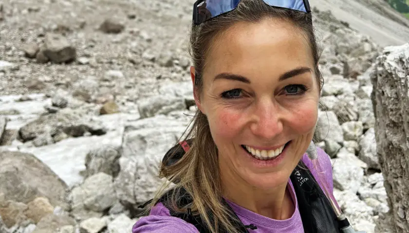 Eva Sperger lächelt in die Kamera, während sie auf einem steinigen Bergpfad unterwegs ist.