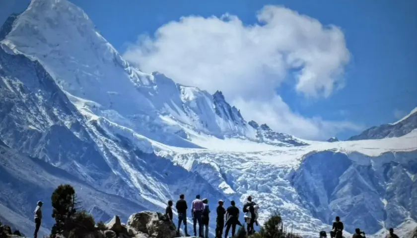Bergsteiger bestaunen die majestätische Rupal-Wand, einen eisigen Riesen unter blauem Himmel.