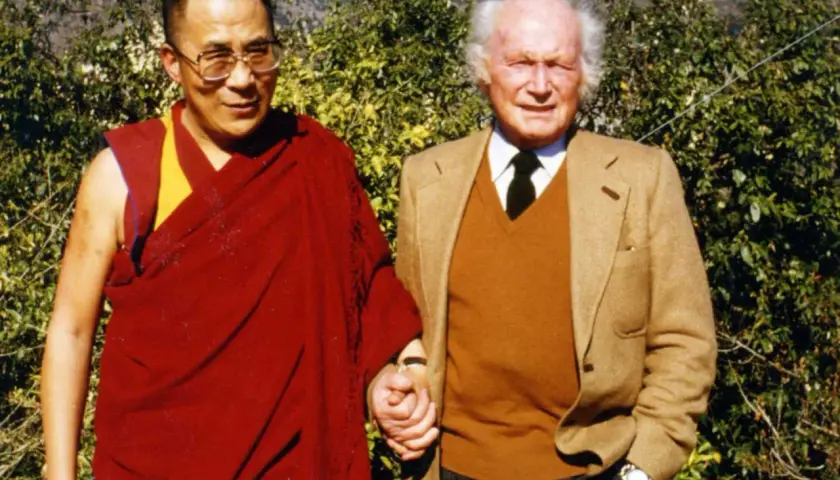 Der Dalai Lama und Heinrich Harrer, ein Freund Tibets, halten Händchen vor üppigem Grün.