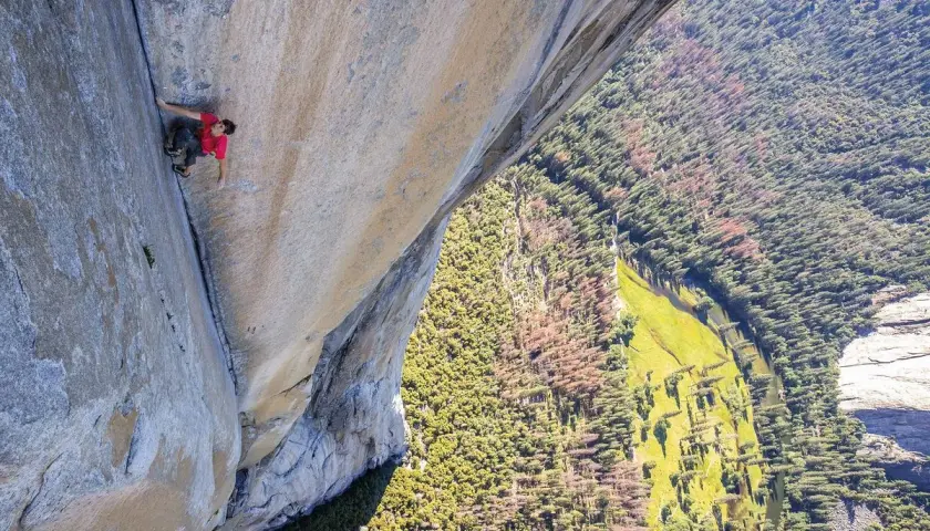 Ein Kletterer bezwingt eine riesige Felswand im Stil des free solo film. Tief unten schlängelt sich ein Fluss durch einen grünen Wald.