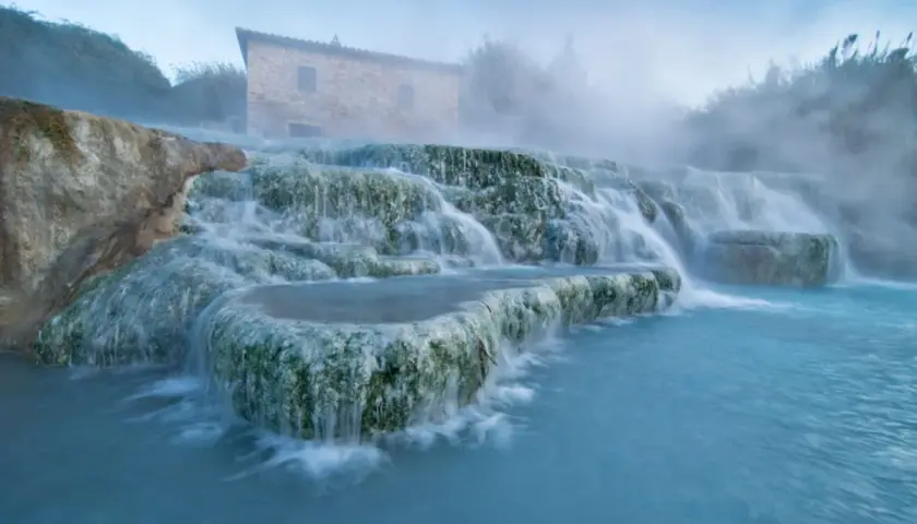 Toskana: malerische schwefelquellen mit einem alten Steinhaus im Hintergrund und dampfendem, türkisfarbenem Wasser.