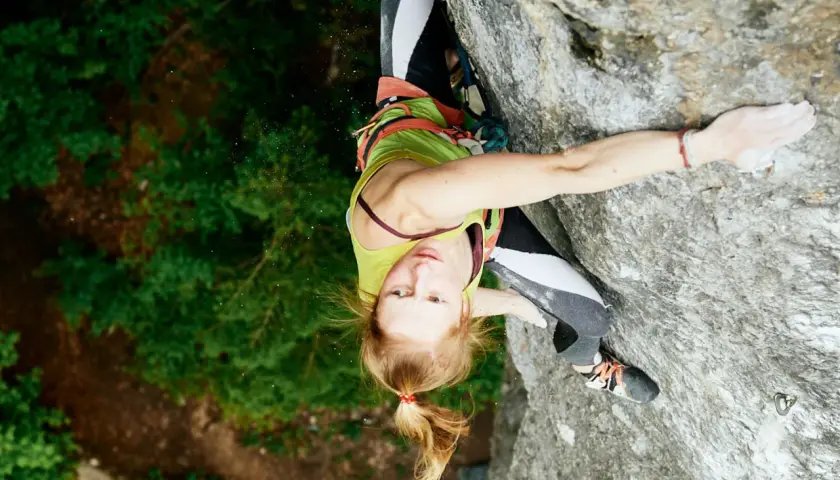 Martina Demmel klettert konzentriert eine Felswand empor, umgeben von üppigem Grün.