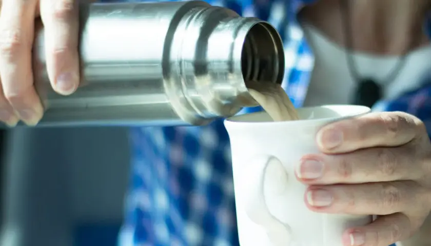 Eine Person gießt Kaffee aus einer Thermoskanne in eine Tasse. Die Thermoskanne reinigen ist wichtig für den Geschmack.
