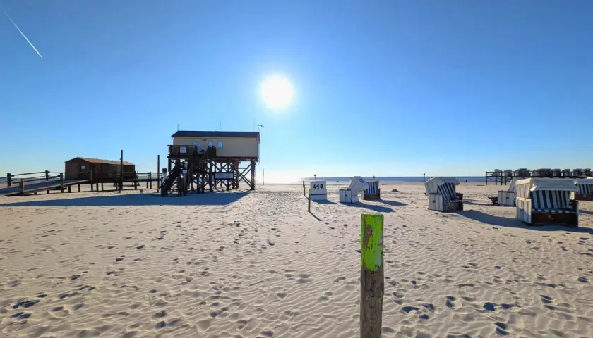 Sonniger Tag am St. Peter-Ording Strand mit Strandkörben und Stelzenhäusern.