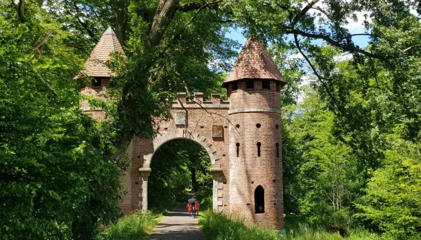 Ein Torbogen mit Türmen, umgeben von üppigem Grün. Ein Radfahrer fährt hindurch. Ein echter Geheimtipp in Wittenberg für Naturliebhaber.