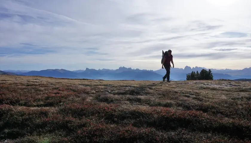 Eine Person wandert im Oktober durch die Alpen. Die Sonne scheint, der Himmel ist leicht bewölkt.