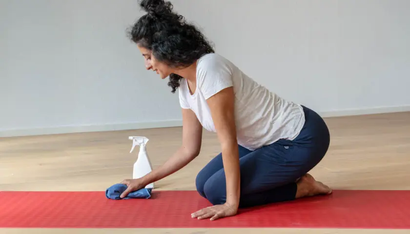 Frau reinigt ihre naturkautschuk yogamatte mit einem Tuch und Sprühflasche.