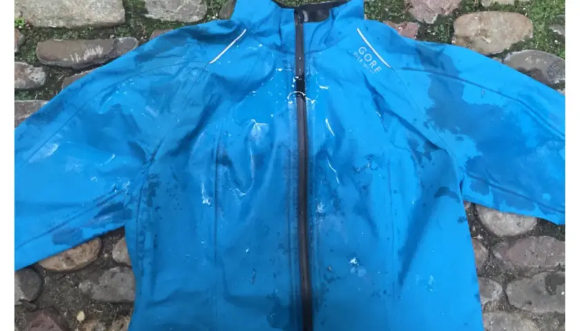 Blaue Gore-Tex Regenjacke mit Wasserflecken, bereit zum Trocknen auf einem steinigen Untergrund.