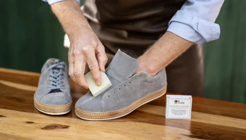 Mann reinigt graue Nubukleder-Sneaker mit einem speziellen Radierer. Die richtige nubukleder pflege erhält die Schuhe.
