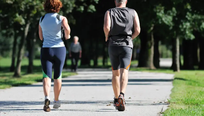 Ein Paar genießt **slow jogging** auf einem Weg im Park. Im Hintergrund eine weitere Person.