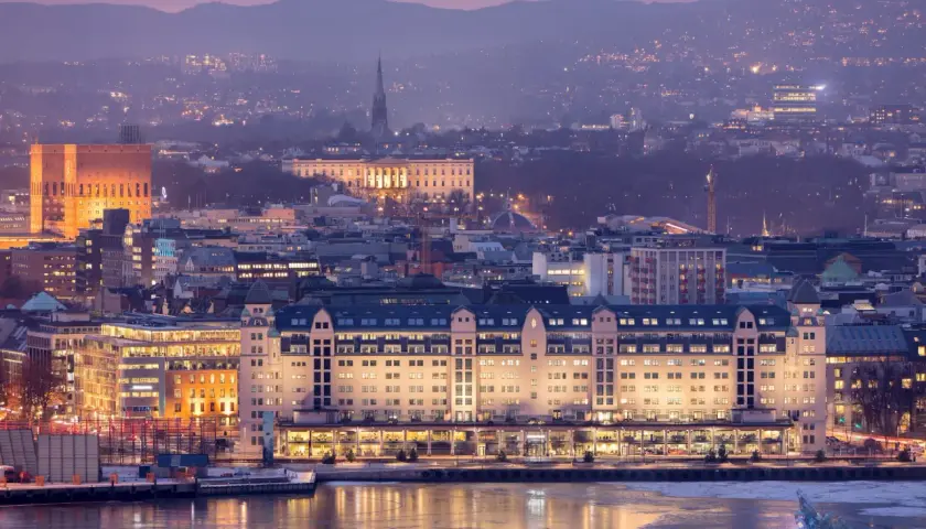 Oslo bei Nacht: beleuchtete Gebäude am Wasser, im Hintergrund die Stadt und Berge. Ein Muss für jeden Oslo-Besucher!