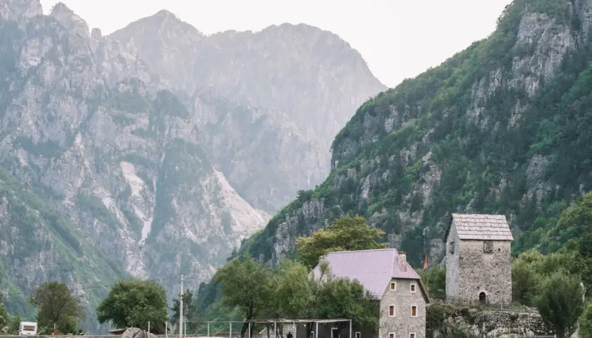 Steinerne Häuser und ein alter Turm in Albanien Theth, umgeben von majestätischen, nebelverhangenen Bergen.