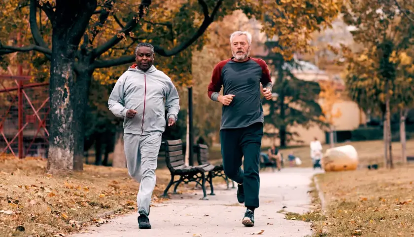 Zwei Männer im Herbstpark trainieren für den Halbmarathon. Sie laufen auf einem Weg, umgeben von bunten Blättern.