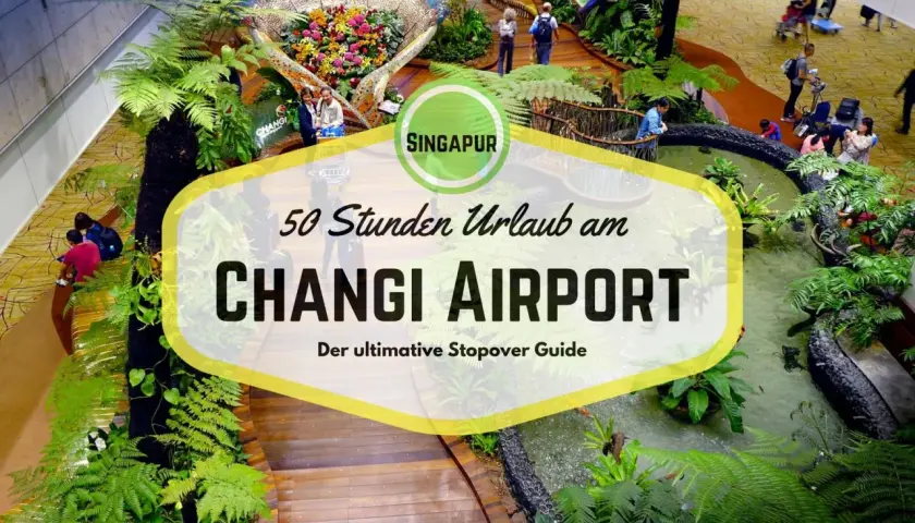 Üppige Pflanzen und ein Wasserfall im **Singapur Flughafen** Changi. Ein Schild wirbt für "50 Stunden Urlaub am Changi Airport".