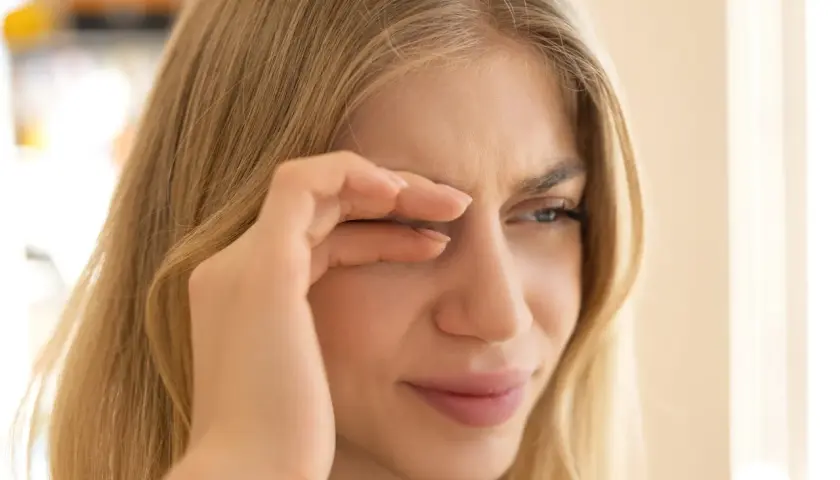 Junge Frau reibt sich die Augen, weil sie flimmern vor den Augen hat. Wahrscheinlich hat sie zu wenig getrunken.