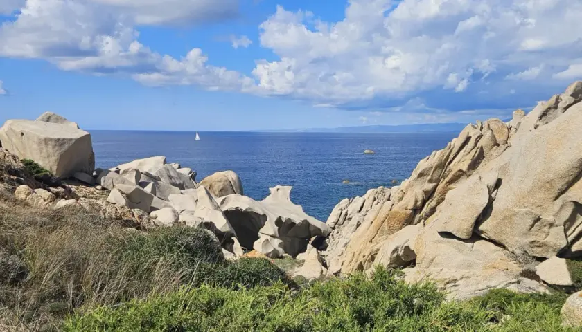 Felsformationen am Capo Testa, Sardinien, mit Blick auf das blaue Meer und eine einsame Segelyacht.