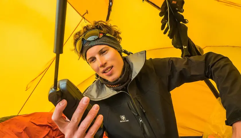 Jost Kobusch im gelben Zelt, hält ein Gerät in der Hand. Handschuhe hängen über ihm.