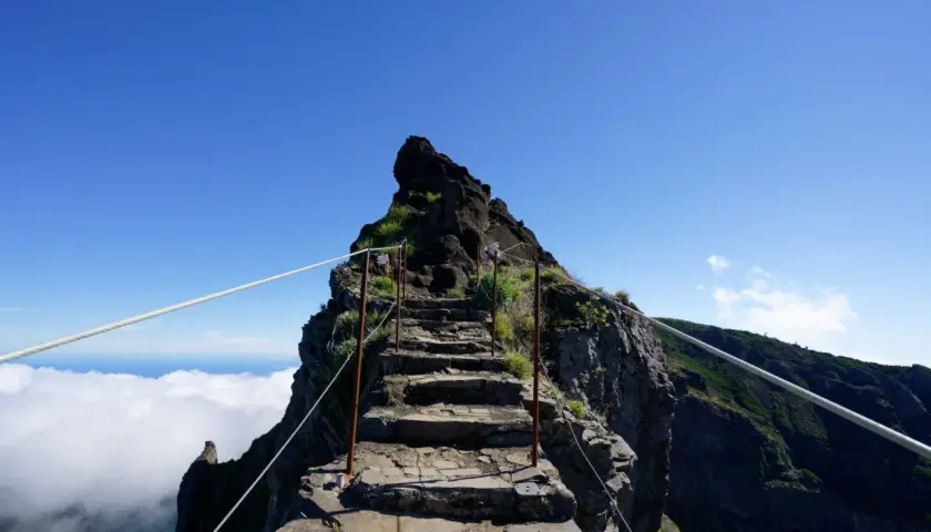 Steile Steintreppe, die sich den Berg hinaufwindet, mit Seilen gesichert. Eine Himmelsleiter auf Madeira, die über den Wolken in den blauen Himmel führt.