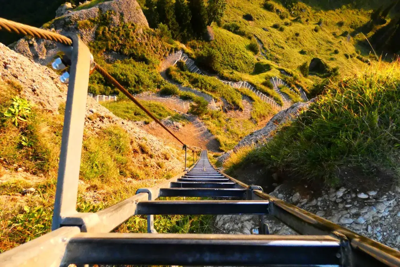 Lange Leiter führt steil einen Berg hinauf. Ein Drahtseil sichert den Weg.