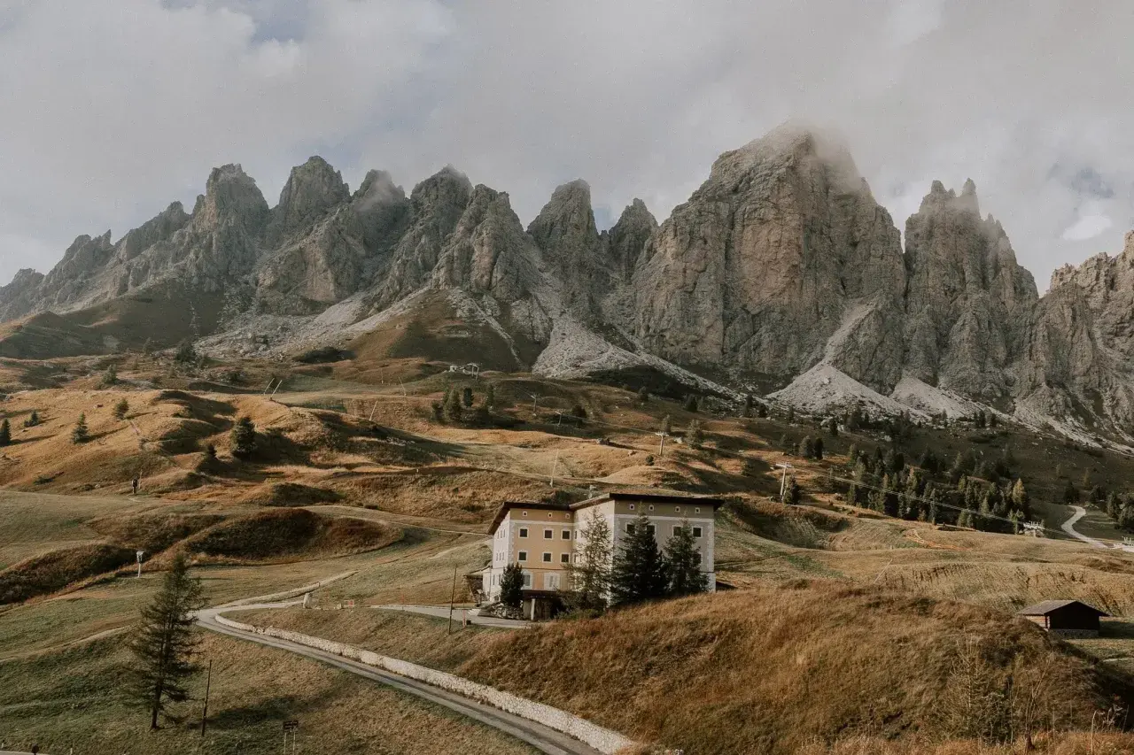 Majestätische Berge im Val di Funes, ein Hotel auf einem Hügel, umgeben von herbstlichem Gras und einer Straße.