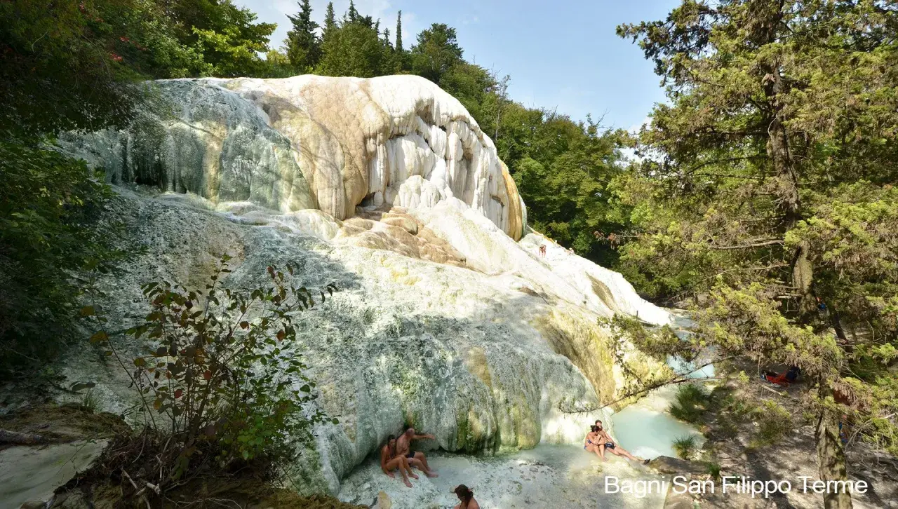 Natürliche Kalkformationen und türkisfarbene Thermalbecken in Bagni San Filippo. Menschen entspannen sich im warmen Wasser.