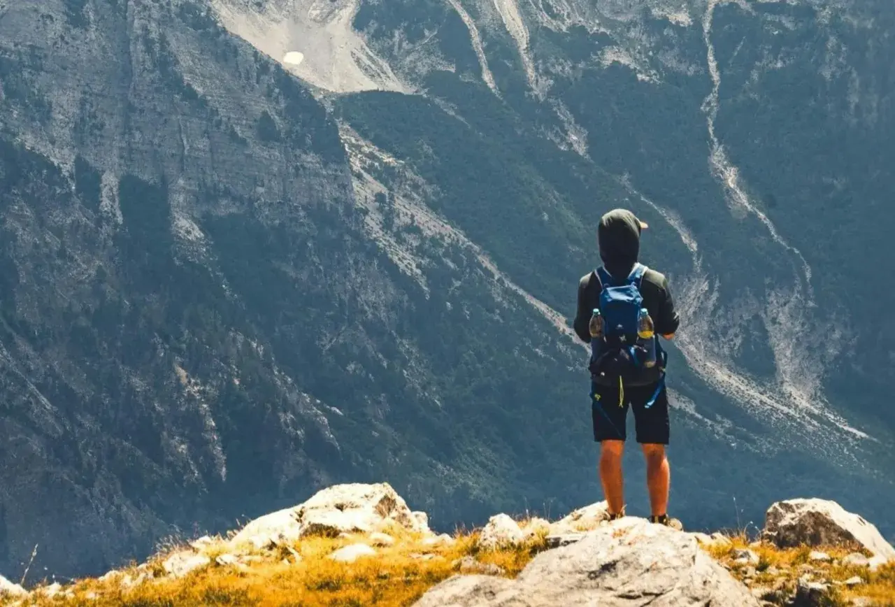 Ein Wanderer mit Rucksack steht auf einem Felsen und blickt in die majestätische Berglandschaft Albaniens.