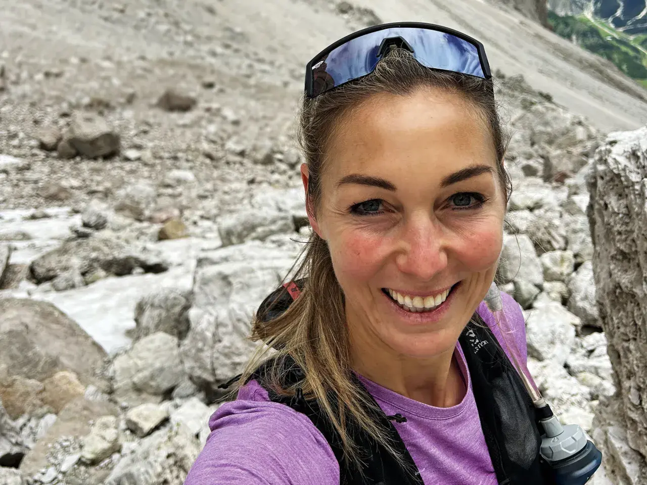 Eva Sperger lächelt in die Kamera, während sie auf einem steinigen Bergpfad unterwegs ist.