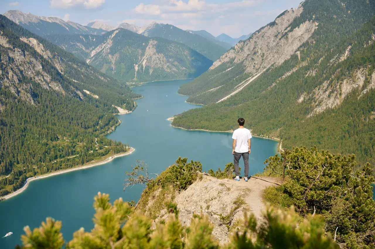 Mann genießt atemberaubende Aussicht beim Plansee Wandern. Türkisblaues Wasser, grüne Wälder und majestätische Berge.
