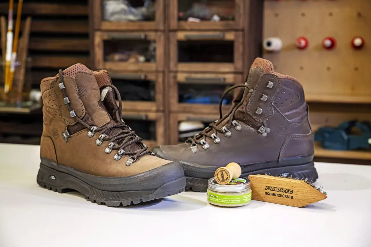 Zwei braune Wanderschuhe bereit zum Reinigen, daneben eine Dose Wachs und eine Bürste.