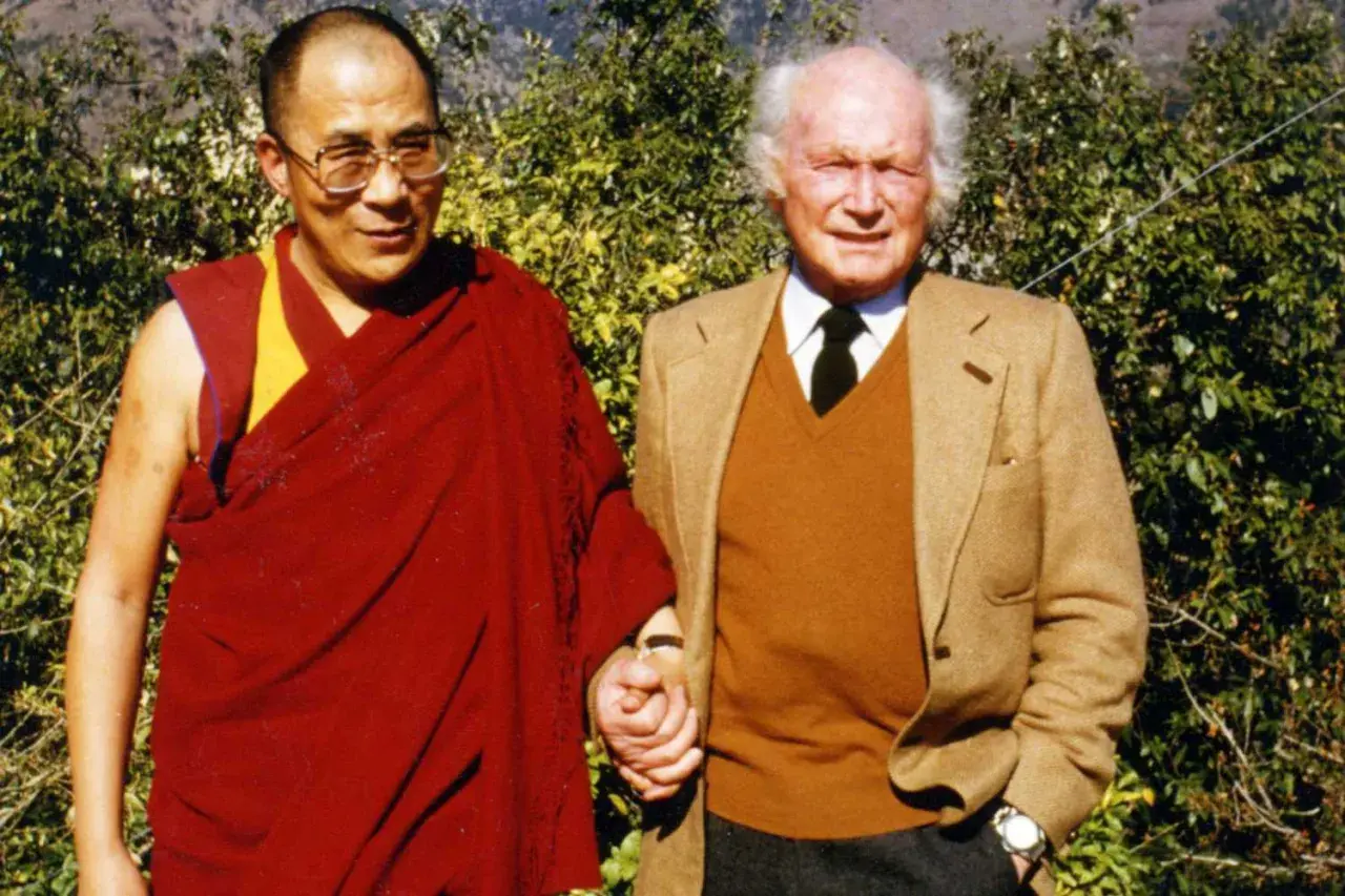 Der Dalai Lama und Heinrich Harrer, ein Freund Tibets, halten Händchen vor üppigem Grün.