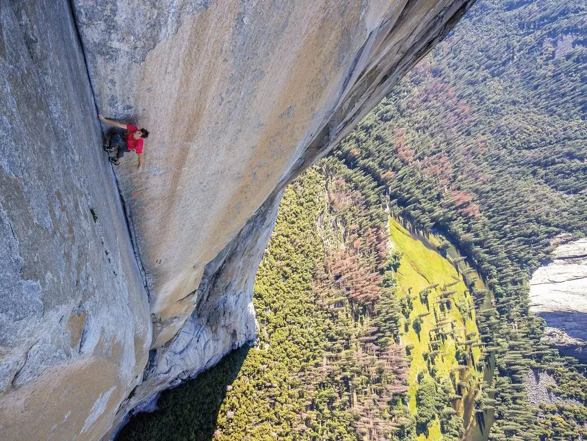Ein Kletterer bezwingt eine riesige Felswand im Stil des free solo film. Tief unten schlängelt sich ein Fluss durch einen grünen Wald.