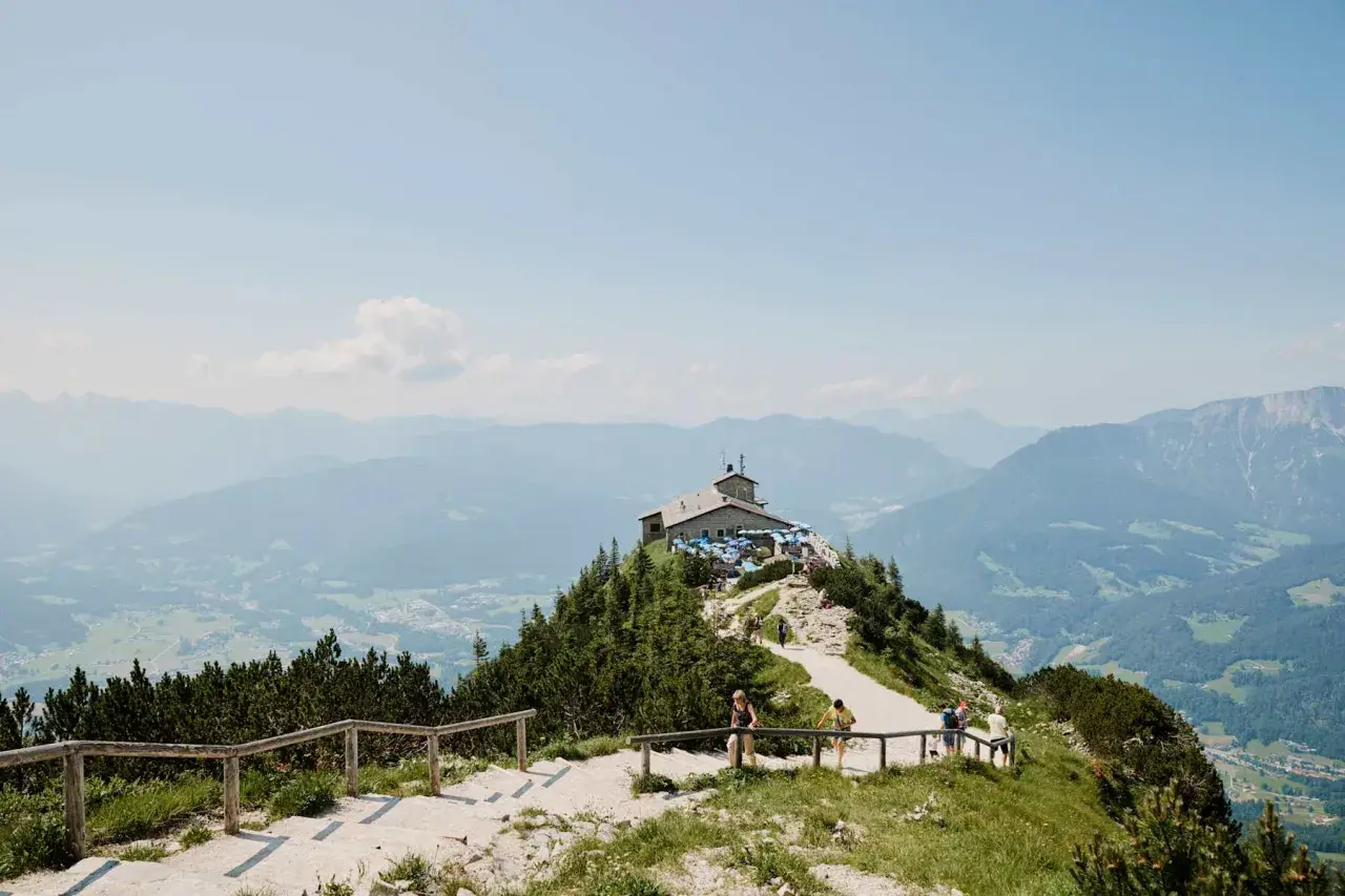 Auf einer Kehlsteinhaus Wanderung genießt man diese Aussicht: Ein Haus thront auf einem Berg, umgeben von grünen Wäldern und majestätischen Alpen.