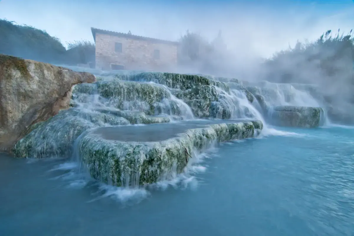Toskana: malerische schwefelquellen mit einem alten Steinhaus im Hintergrund und dampfendem, türkisfarbenem Wasser.