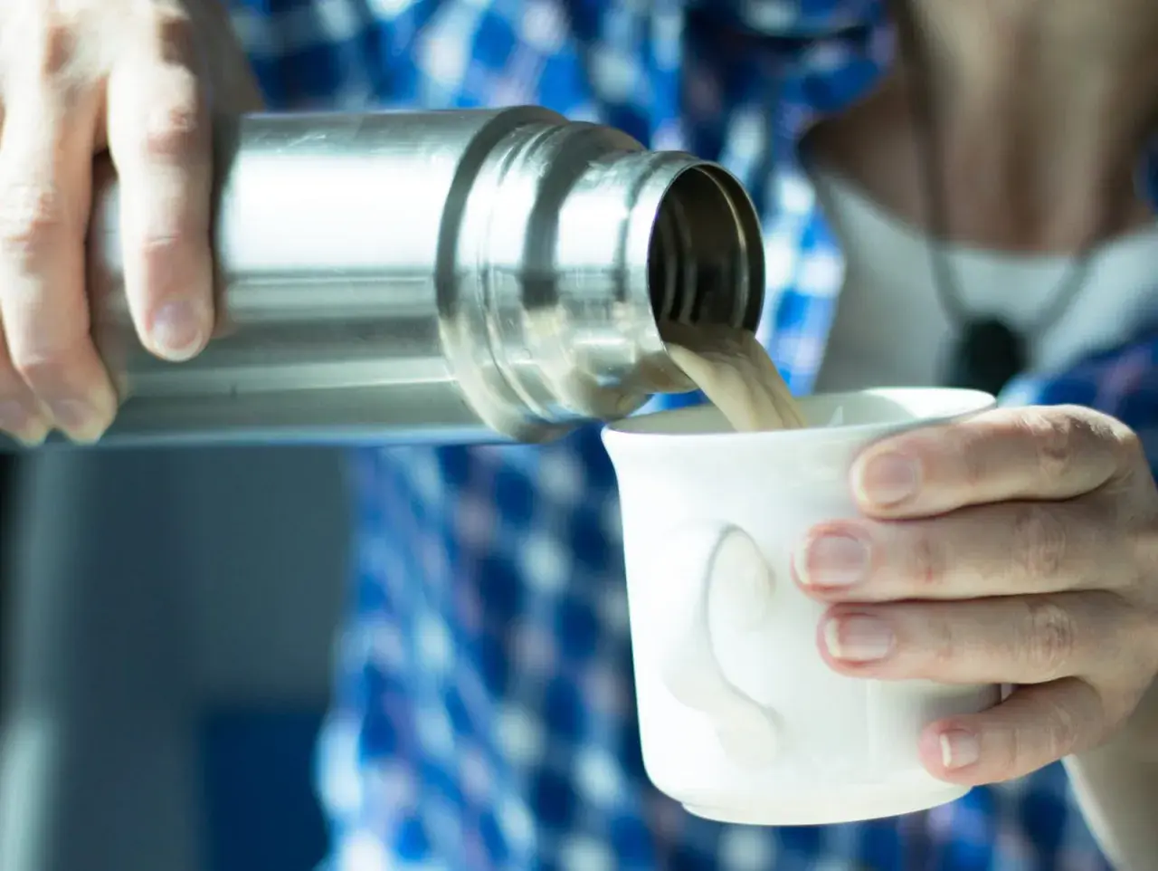 Eine Person gießt Kaffee aus einer Thermoskanne in eine Tasse. Die Thermoskanne reinigen ist wichtig für den Geschmack.