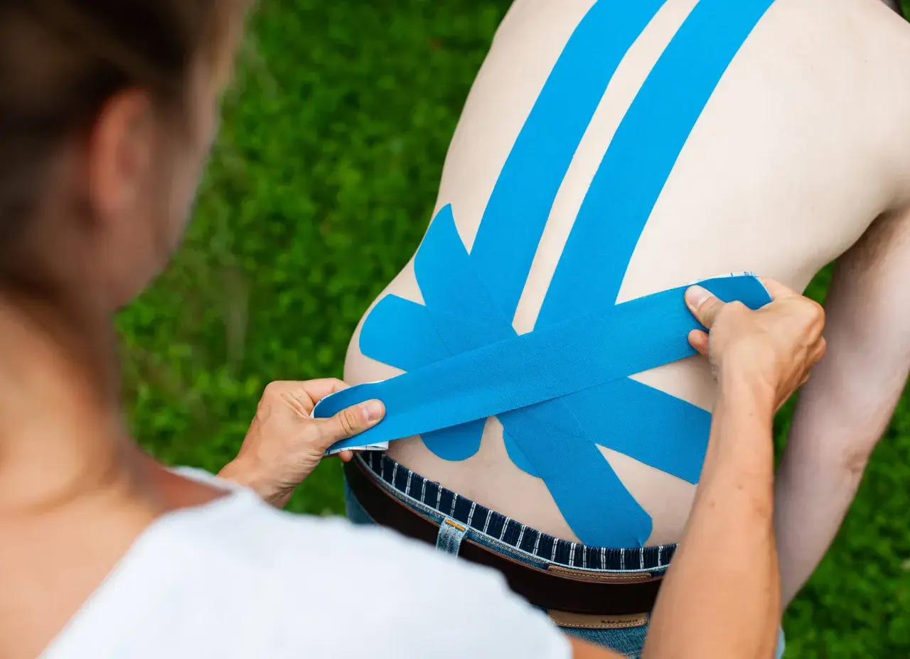 Eine Person legt blaues Tape auf den Rücken eines Mannes. Das Tape dient als Unterstützung und zur Linderung von Schmerzen.