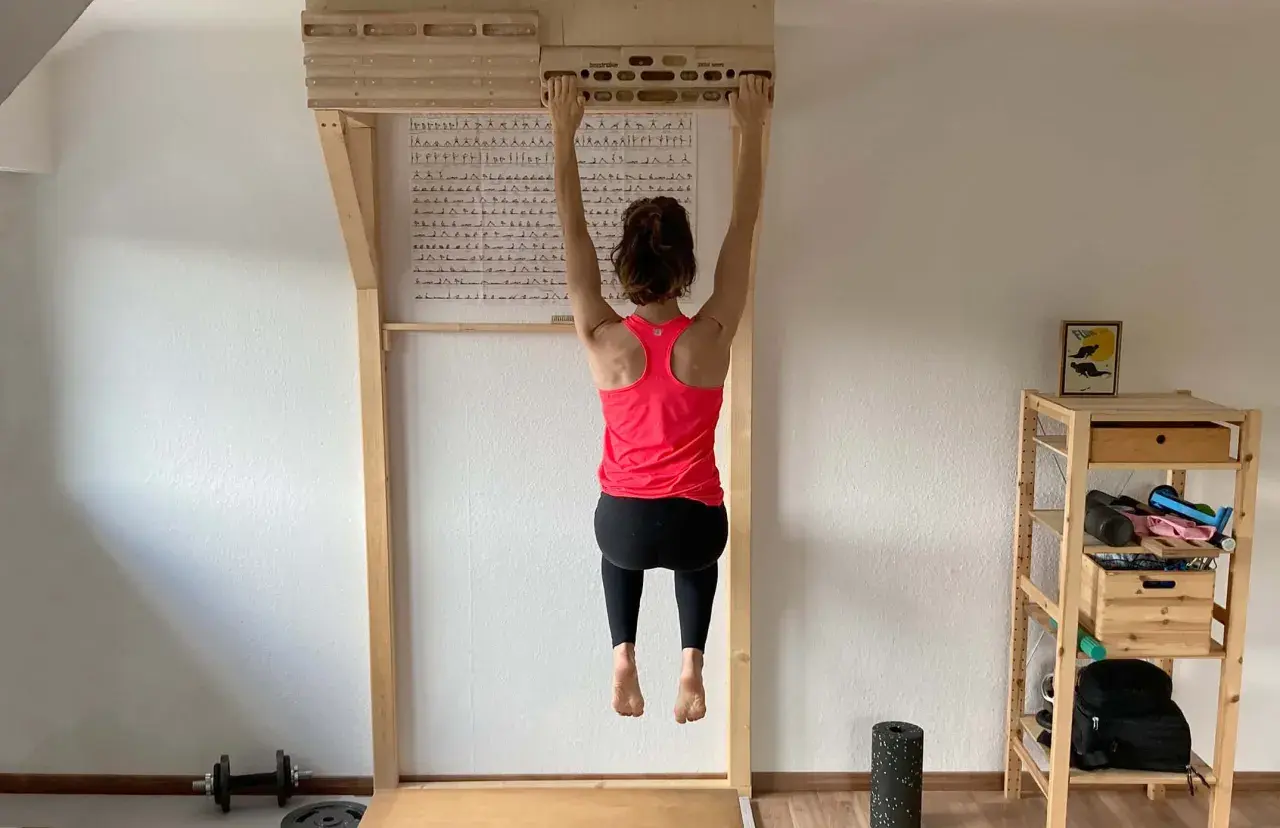 Frau hängt an einem Hangboard für intensives **Hangboard Training**. Trainingsplan hängt an der Wand.