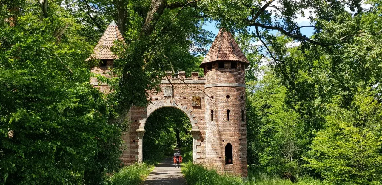Ein Torbogen mit Türmen, umgeben von üppigem Grün. Ein Radfahrer fährt hindurch. Ein echter Geheimtipp in Wittenberg für Naturliebhaber.