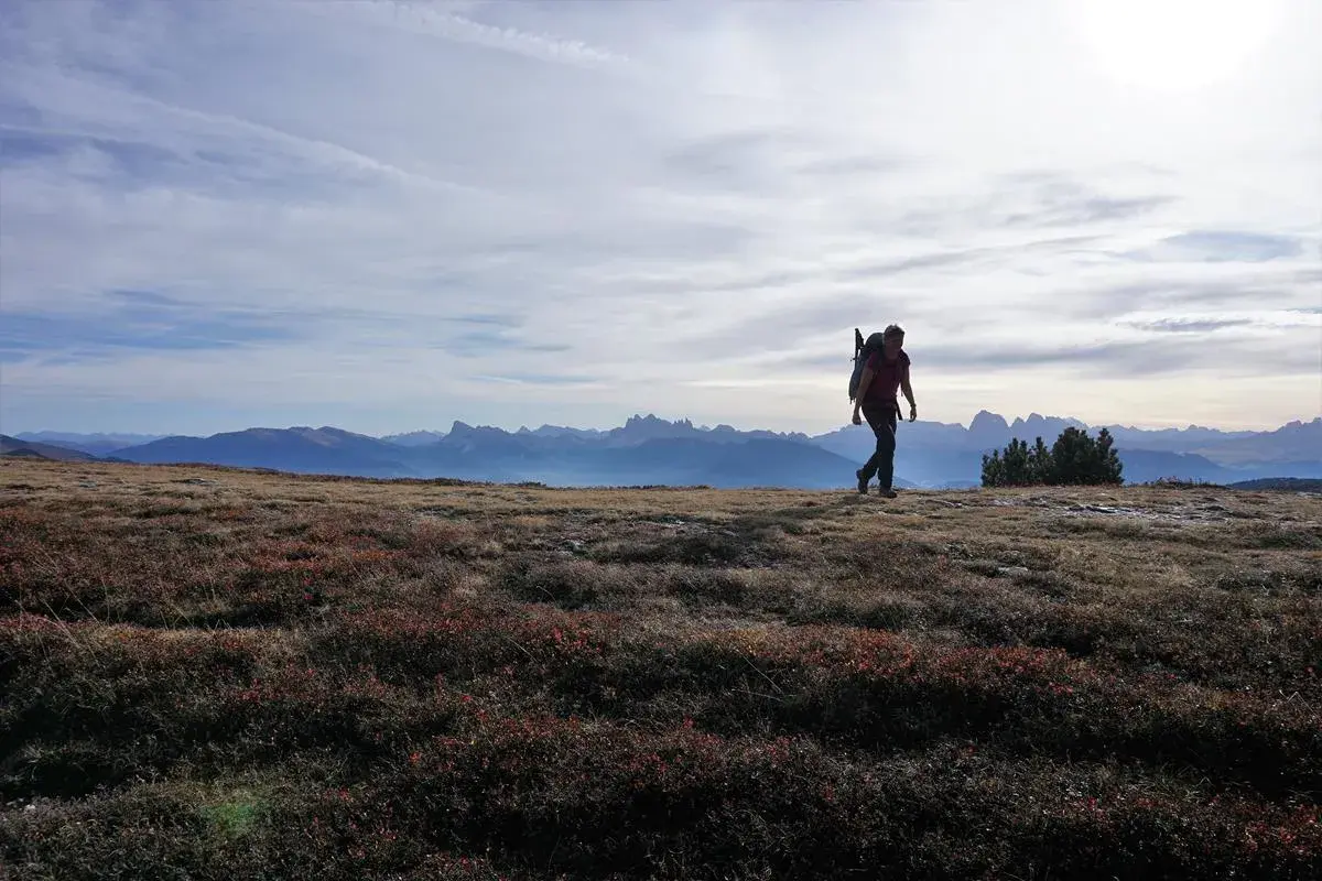 Eine Person wandert im Oktober durch die Alpen. Die Sonne scheint, der Himmel ist leicht bewölkt.