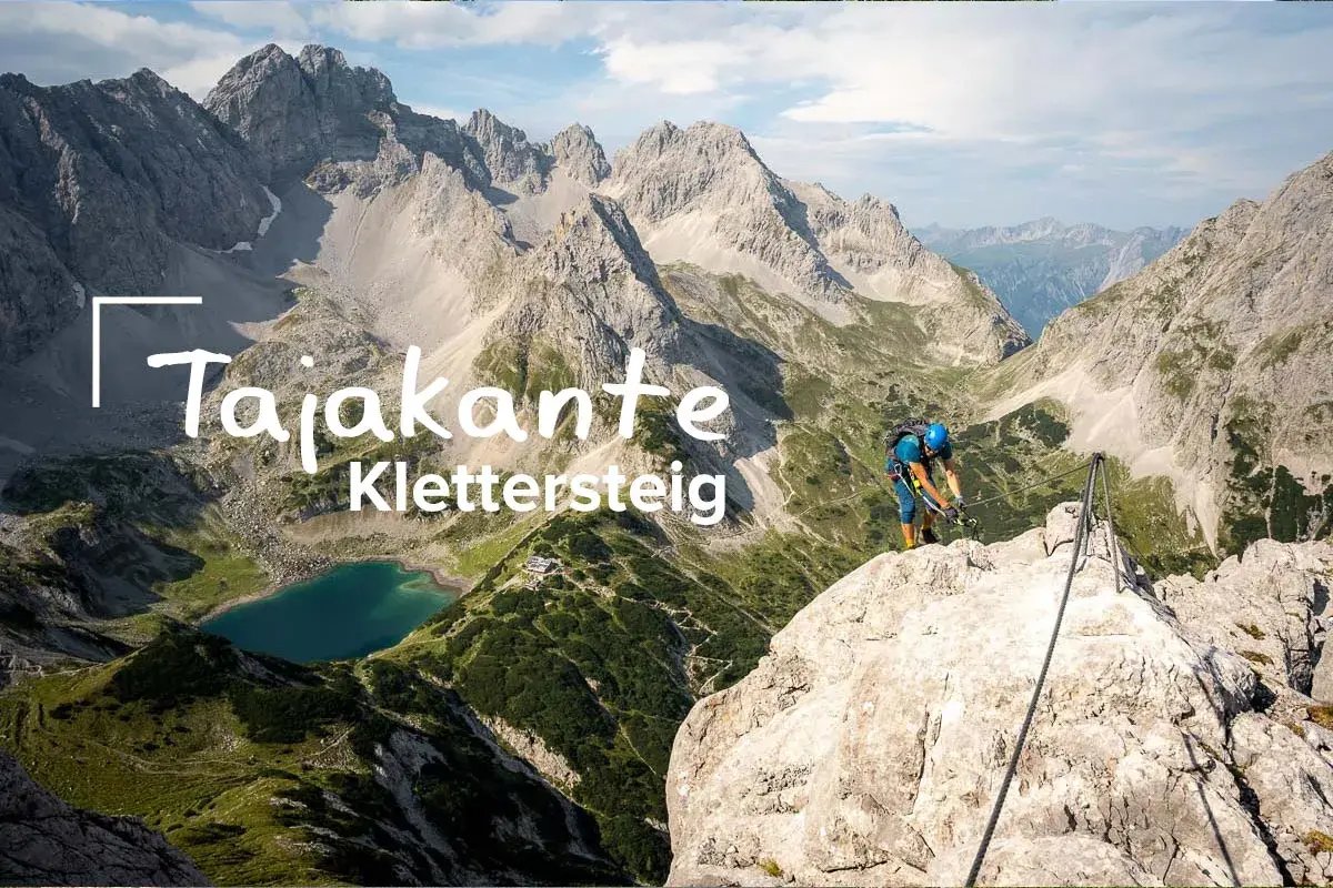 Ein Kletterer sichert sich am Tajakante Klettersteig mit Blick auf einen Bergsee.