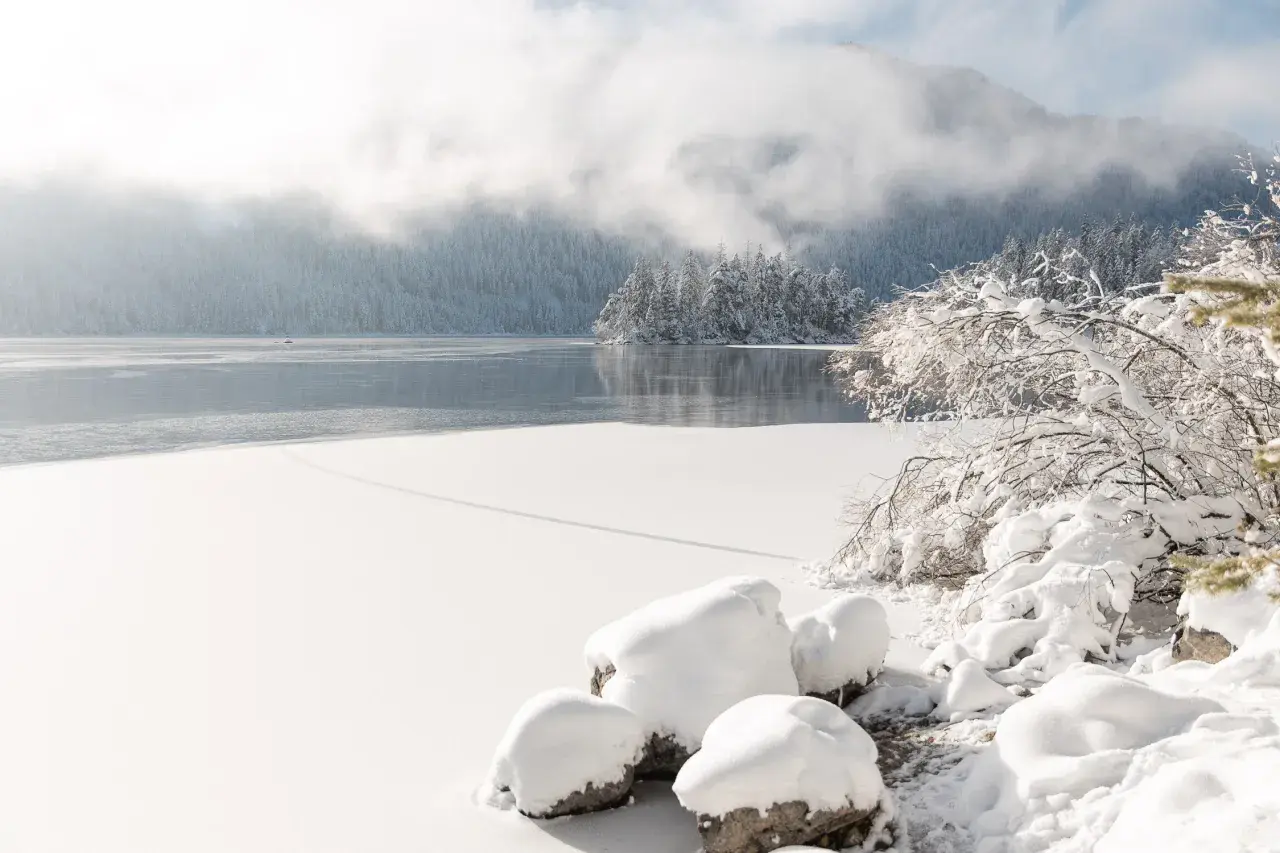 Eibsee winter: Eisbedeckter See, verschneite Bäume und Berge im Nebel. Ein friedlicher Anblick der Natur.